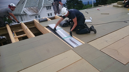 Arbeiter installieren Dachplatten auf dem Gerüst eines Hauses.